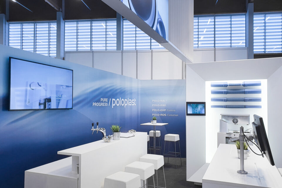 Kommunikationszone am POLOPLAST-Messestand mit Theke, Screens und Produktpräsentation der Systeme POLO-KAL, POLO-KWL, POLO-EHP Control und POLO-RDS Evolution in klarer, technikorientierter Messestandgestaltung.