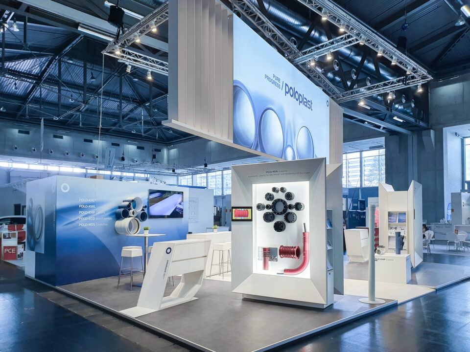 Messestandansicht mit beleuchtetem Produktdisplay für innovative Rohrlösungen, großem Markenbanner und klar strukturiertem Raumdesign für Fachgespräche.